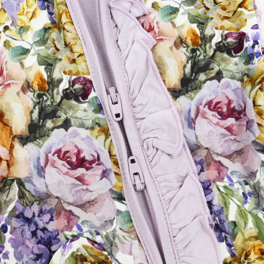 Close-up of a floral fabric garment with a lavender ruffled zipper running vertically through the center. The background fabric features a watercolor-style rose and floral print in soft pink, purple, yellow, and green tones.