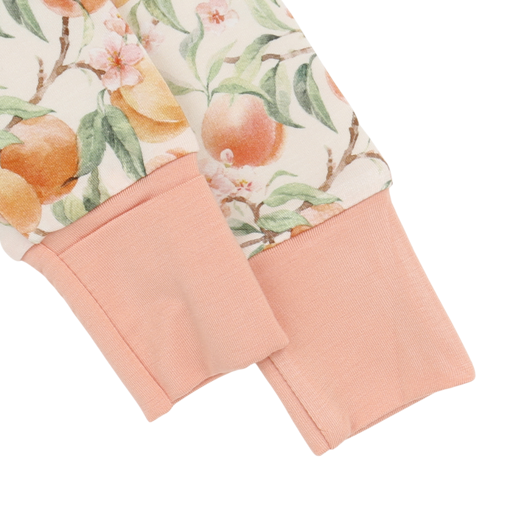 Close-up of a garment with a floral peach pattern and pink cuffs on a white background