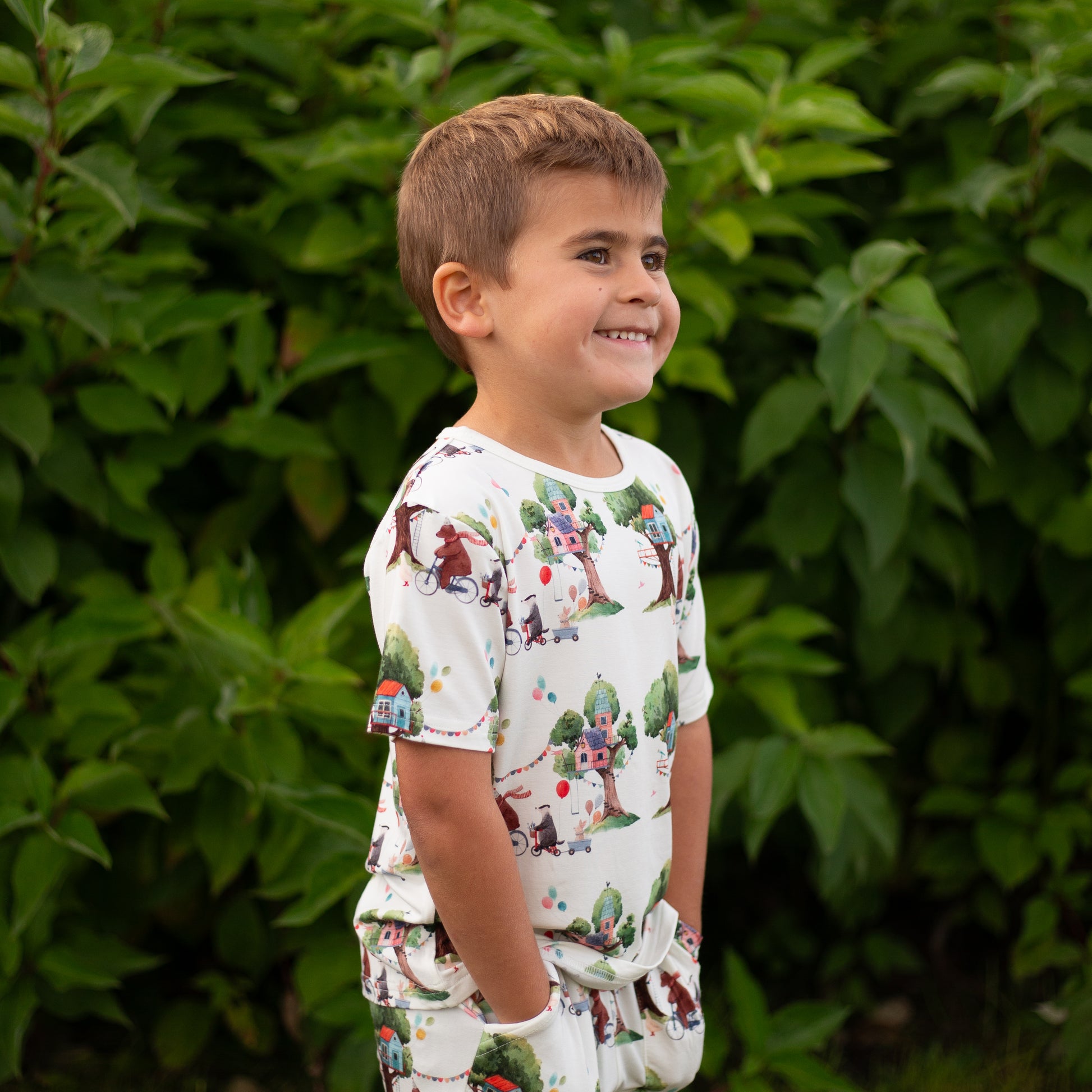 Child wearing a patterned outfit standing in front of green foliage