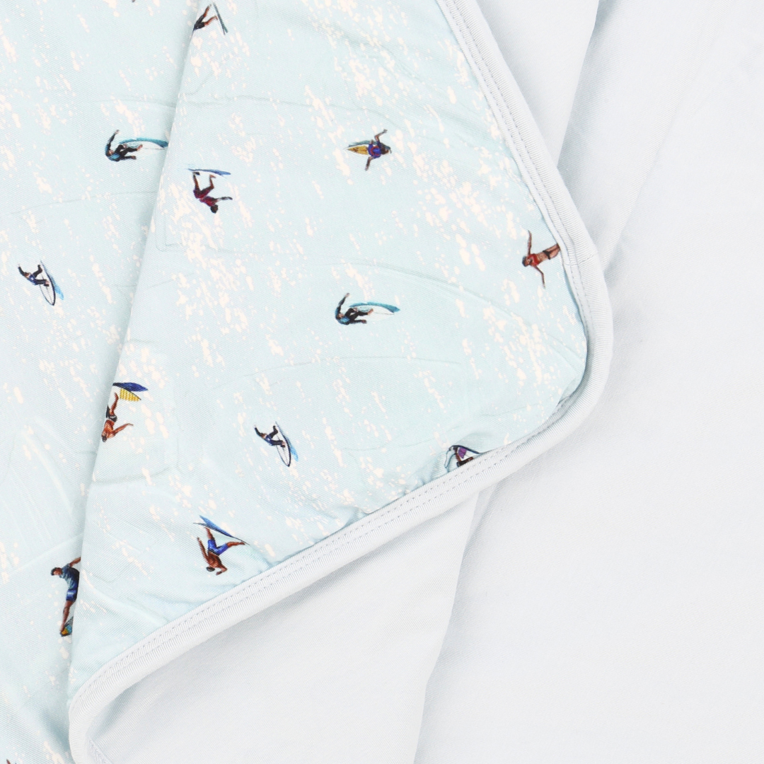 Light blue fabric with small colorful patterns of people on surfboards, folded neatly.