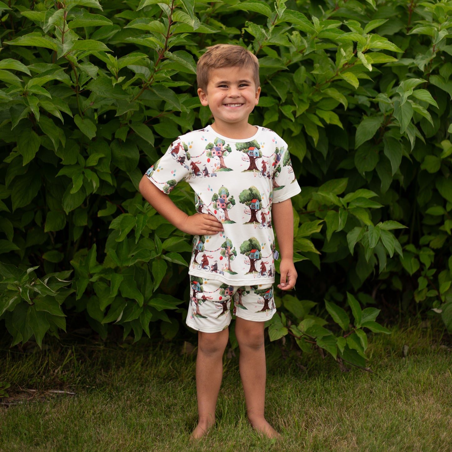 Child wearing a patterned outfit standing in front of green foliage