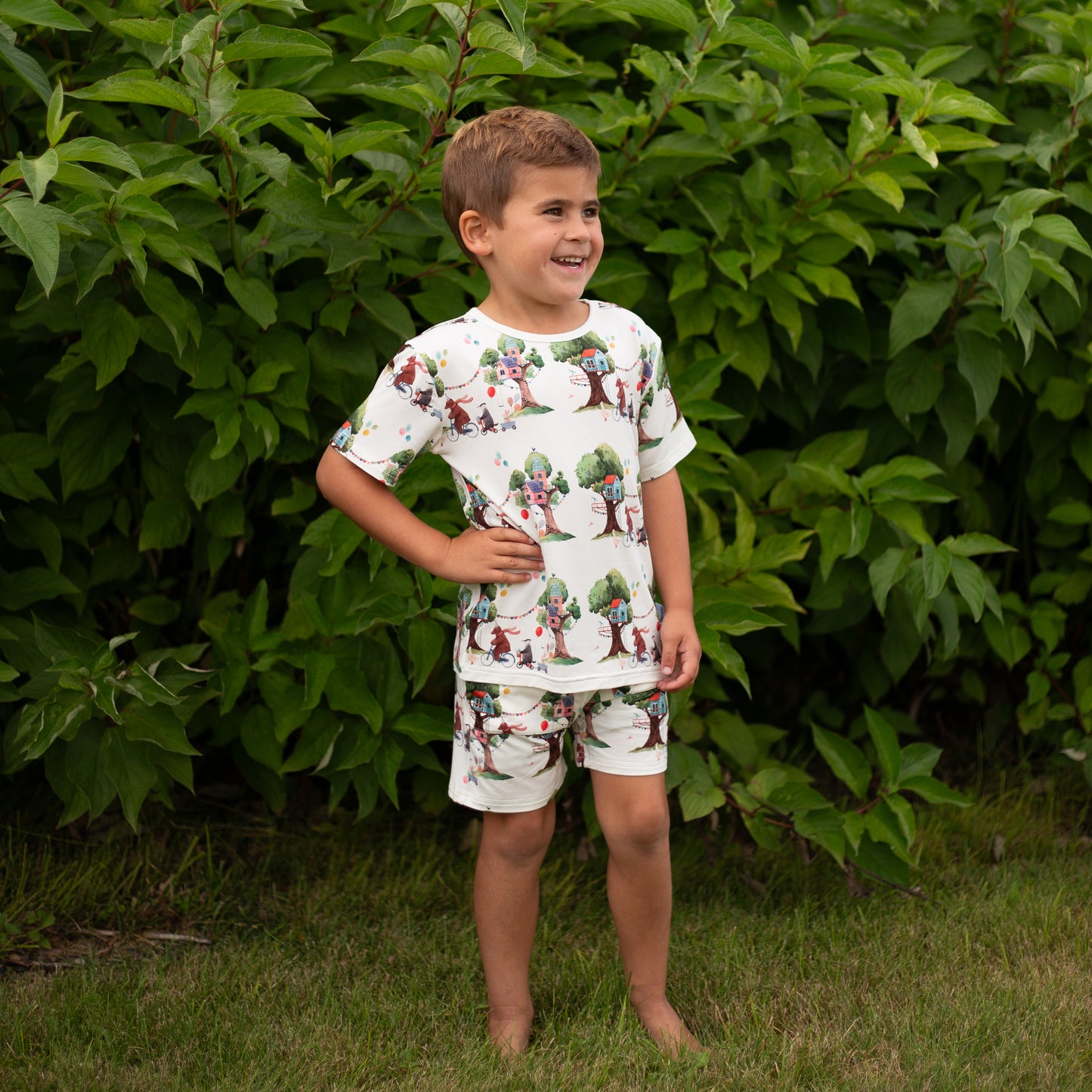 Child wearing a patterned outfit standing in front of green foliage