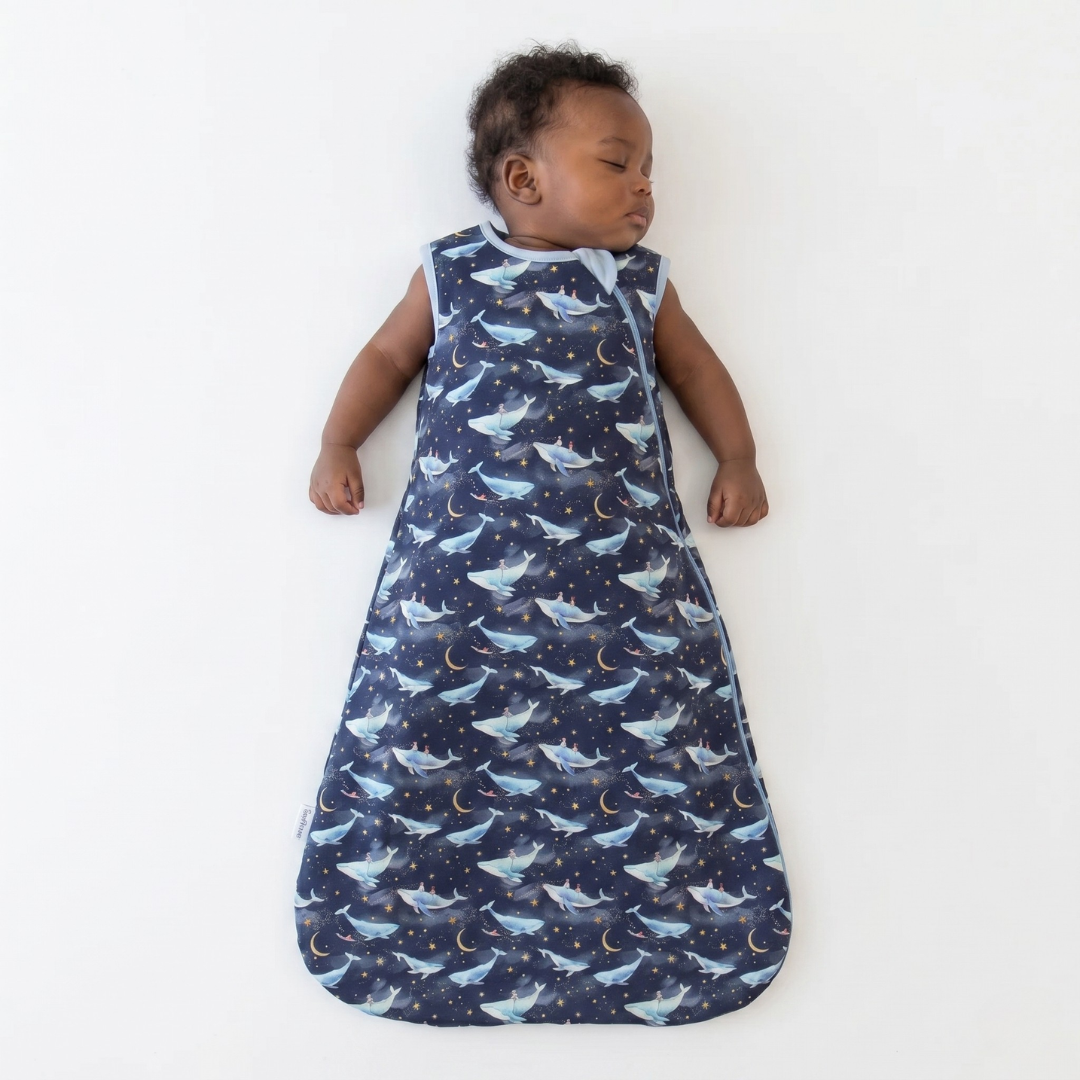 Baby sleeping in a navy blue sleep bag with whale pattern on a white background