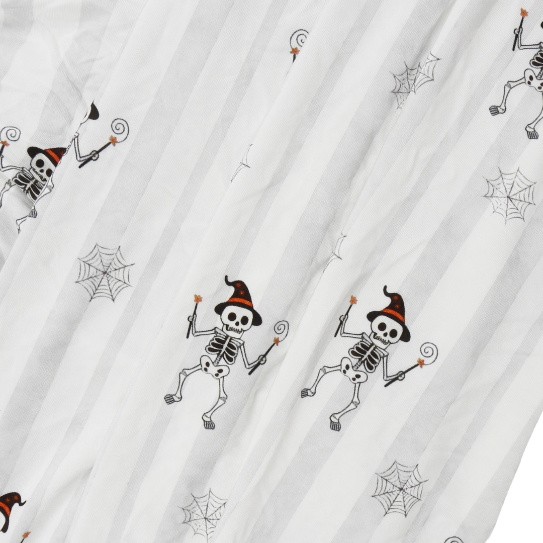 White striped fabric with a repeating pattern of cartoon skeletons wearing orange and black witch hats, holding wands, and surrounded by gray spiderwebs.