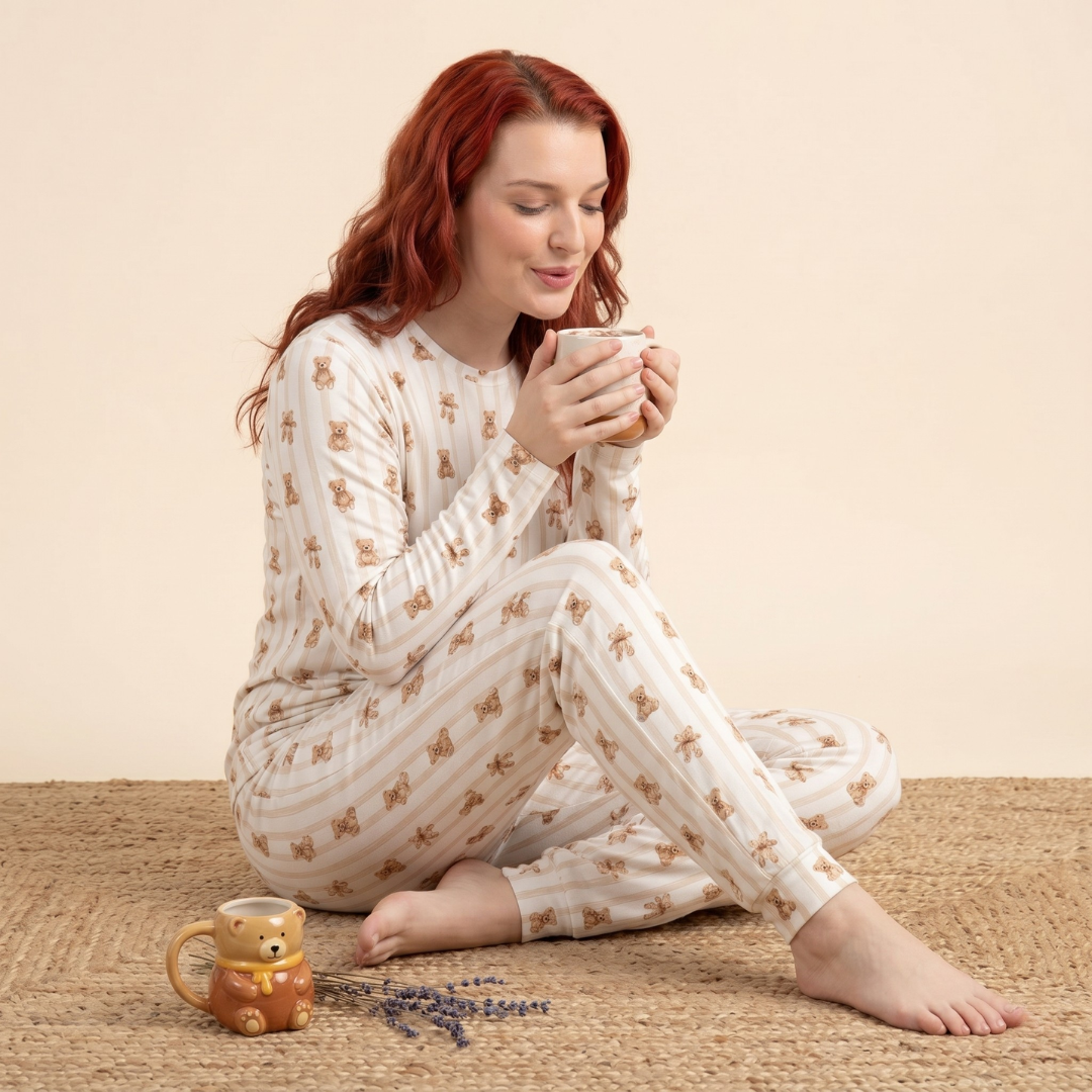 Woman in white pajamas with brown bear pattern sitting on a carpet holding a mug.