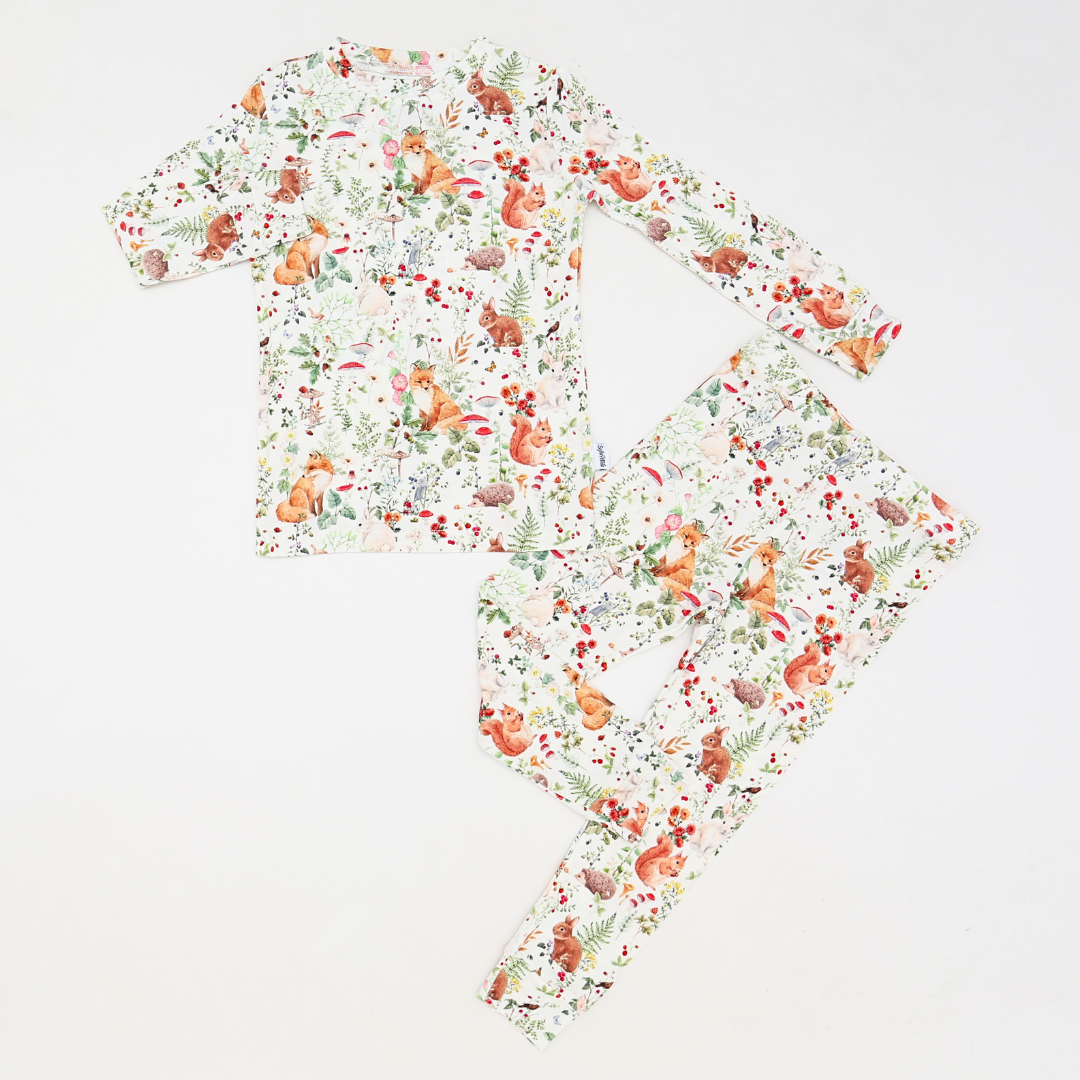 Children’s two-piece pajama set made from bamboo fabric, laid flat on a white background. The set features a woodland animal print with foxes, squirrels, rabbits, mushrooms, and botanical elements in soft, earthy colors.
