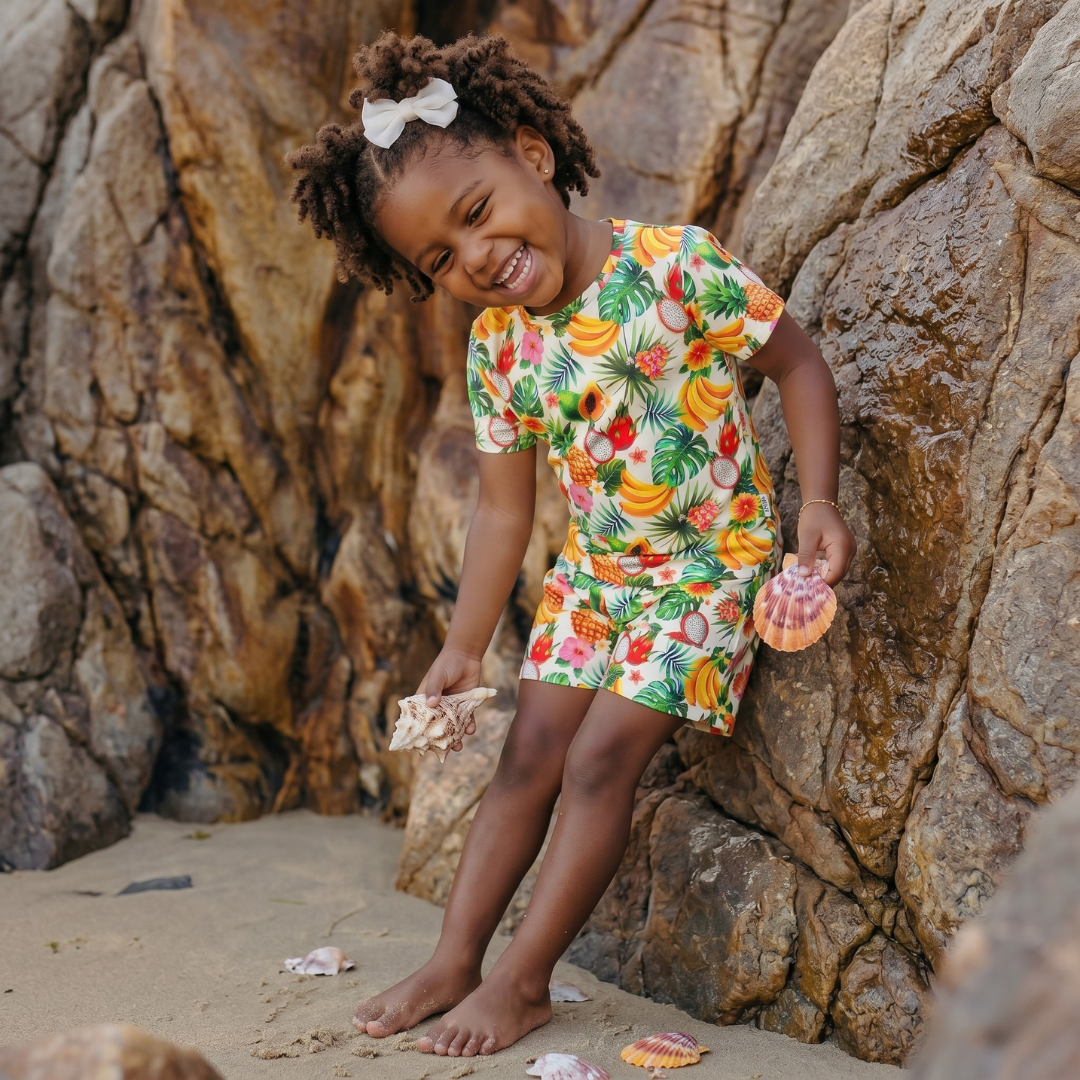 Young girl in a colorful tropical dress standing on a rocky beach.